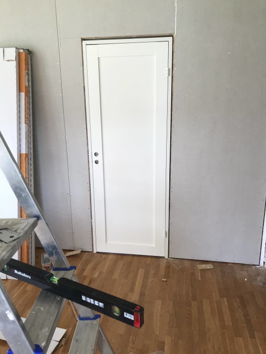 Nyligen installerad vit innerdörr i ett rum under renovering med synlig stege och våg.