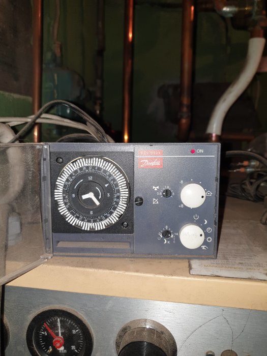 Reglagepanel på en panna med inställningsrattar för temperatur och timers, med kopparledningar i bakgrunden.