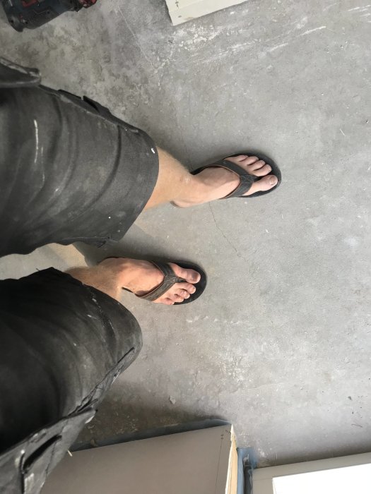 Vy nedåt på en persons fötter i flip-flops på ett betonggolv, symboliserar avslut på hårt arbete.