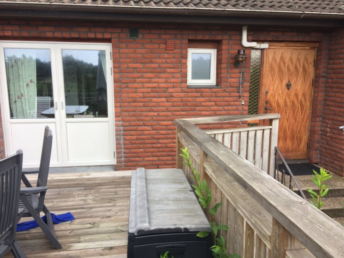 Trädäck med träräcke framför husfasad i tegel, ytterdörr i trä och sidoljus med kondensation.