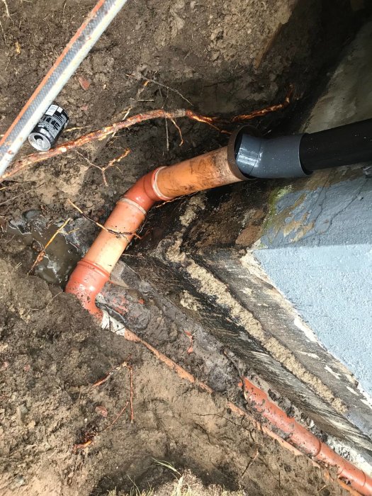 Grundmur med synliga skador och rörledning i utgrävd mark.