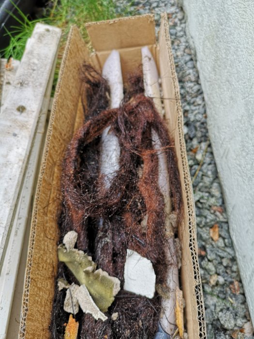 Brunt, hårigt material med tjärliknande lukt och vit isolering i en kartong, använd som drev från 60-talets byggnad.
