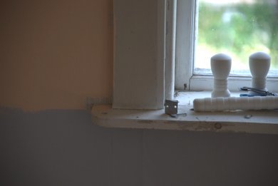 Et malt vinduskarme i et eldre hus under oppussing, med to hvite lysestaker plassert på karmen.