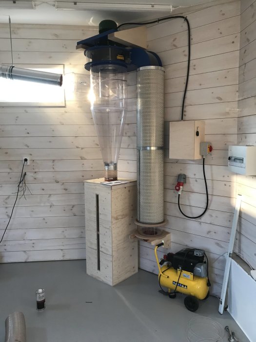 Anpassad spånsugsanläggning med genomskinlig spåntunna och filter, styrenhet och frekvensomformare i verkstadsmiljö.