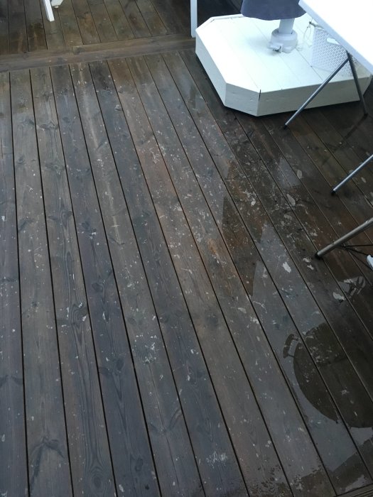 Träaltan med vita fläckar på våta plankor, nära en vit möbel.