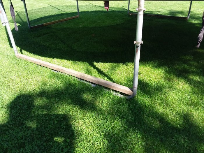 Træpind placeret på tværs som en støtte ved enden af en trampolins ben.