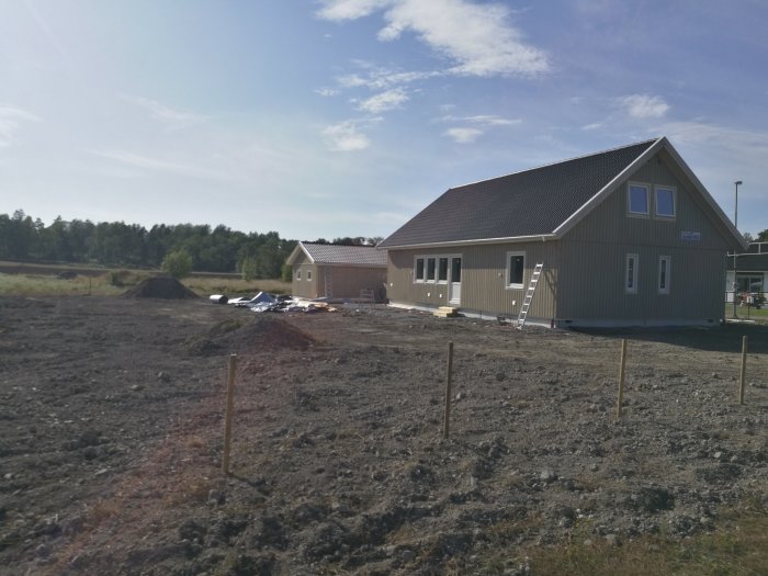 Nybyggt hus med nya takpannor på taket, byggplats i förgrunden med jord och byggmaterial.