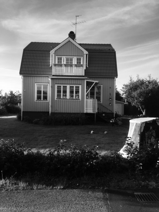 Svartvit bild av ett tvåvåningshus med balkong och lutande tak, potentiell tillbyggnadsplats.