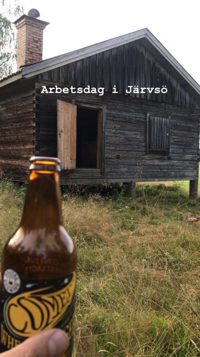 Hand som håller ölflaska framför timmerstuga med texten "Arbetsdag i Järvsö" tryckt på bilden.