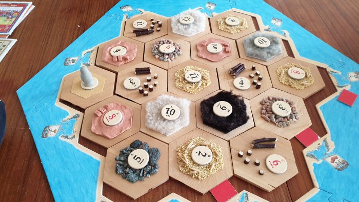 Hemmagjort Settlers of Catan-bräde med oregelbundna hexagonala bitar och olika resurser.