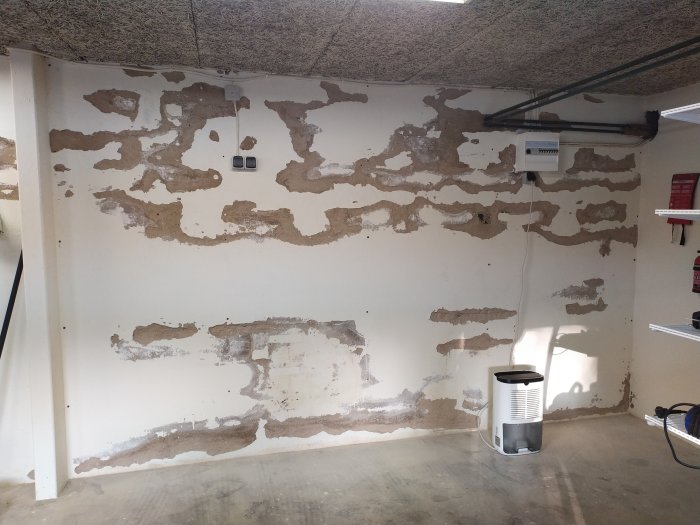 Garagevägg med puts som lossnat på Lecablock, exponerande stenar och ojämn yta.