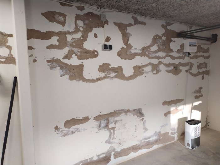 Delvis putsad vägg i ett garage med flagnande ytor på Lecablock, och en avfuktare står på golvet.