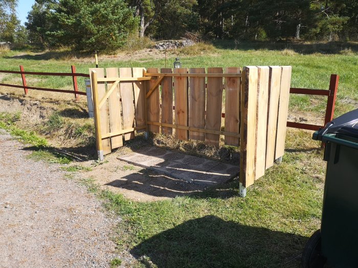 Nybyggt träplank med vankantat virke monterat på en röd staketstolpe vid en grusgång.