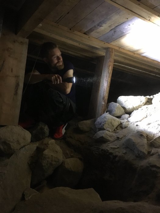 Person som tittar in i en krypgrund fylld med stora stenar genom en öppning i väggen.