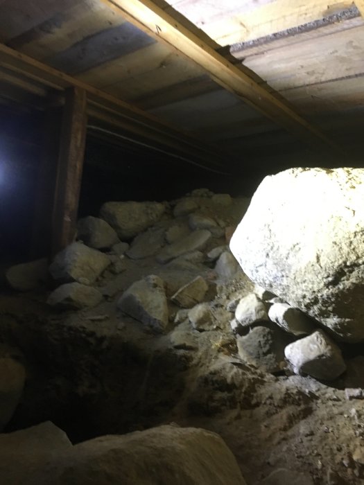 Krypgrund med stora stenar och träbjälkar, potentiellt för omvandling till hel källare.
