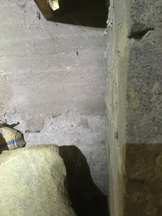Vy genom en lucka i källarväggen mot en krypgrund med stora stenar.