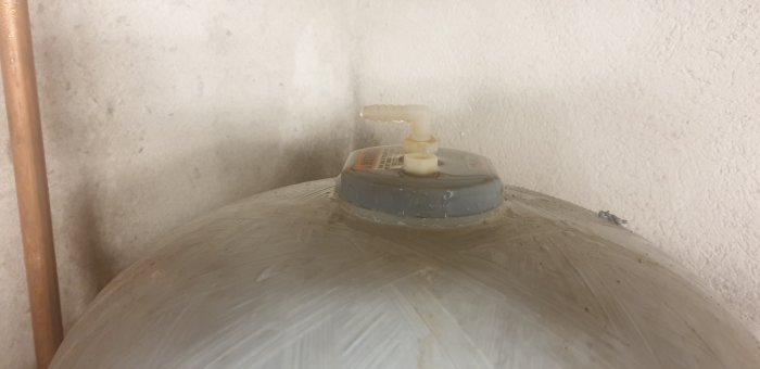 Hydrofor med plastkoppling som läcker vatten, synlig fuktighet runt basen.