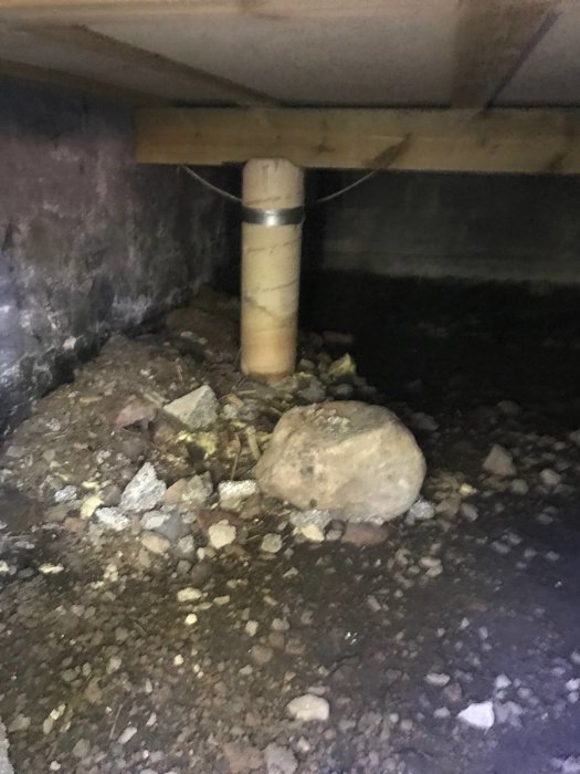 Krypgrund med synliga fuktfläckar, oregelbundna stenar på marken och en stödpelare.