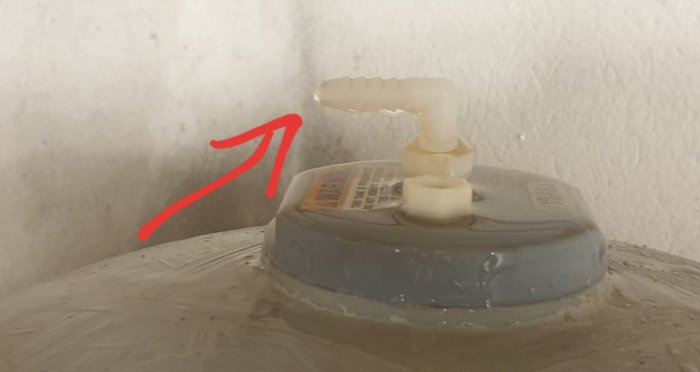 Vattenventil med en utstickande vit pip markerad med en röd pil på en stor behållare.