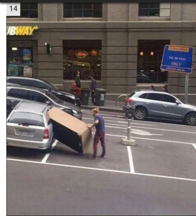 Person försöker få in en stor kartong i en liten bil på en parkeringsplats.