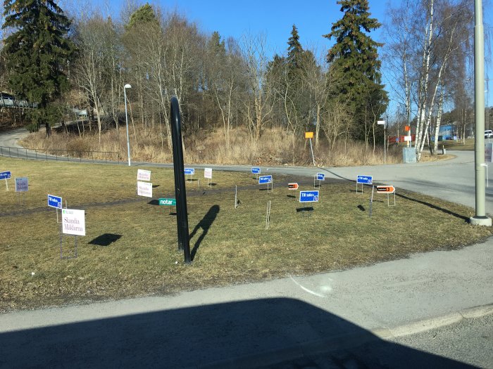 Flera mäklarskyltar placerade på en gräsmatta vid en vägkorsning på en solig dag.