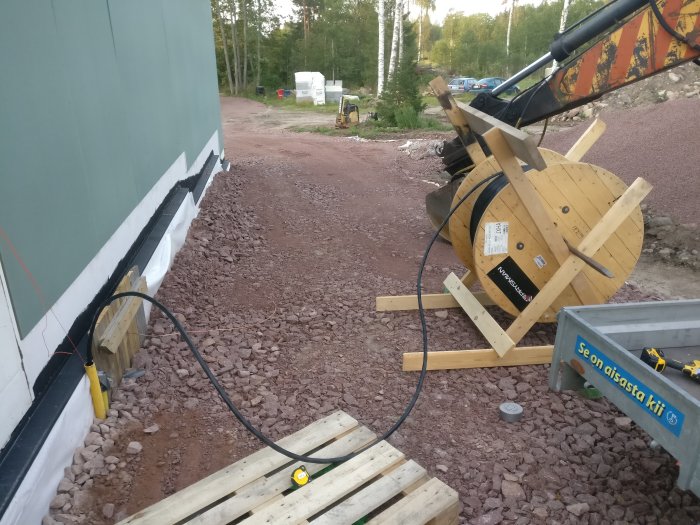 Kabeltrumma och elservis vid en husgrund med byggmaterial och öppen grävd kabeldike.