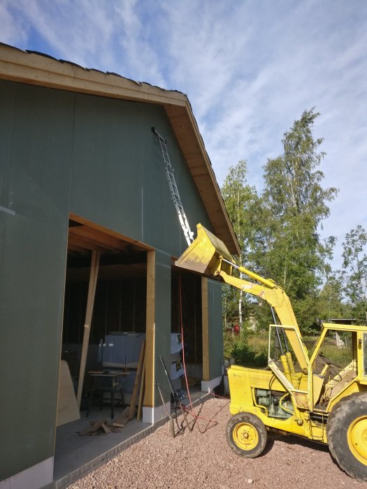 Byggnad under renovering med isolering synlig och gult fordon som hanterar material.