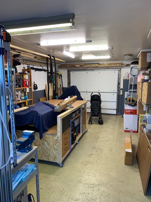 Ett rörigt garage med verktyg, arbetsbänk och en stängd garagedörr som visar ventilationsförhållandena.