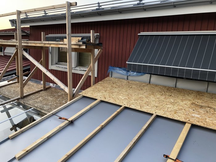 Byggarbetsplats med halvfärdig ställning och skydd över tak med solpaneler på husets baksida.