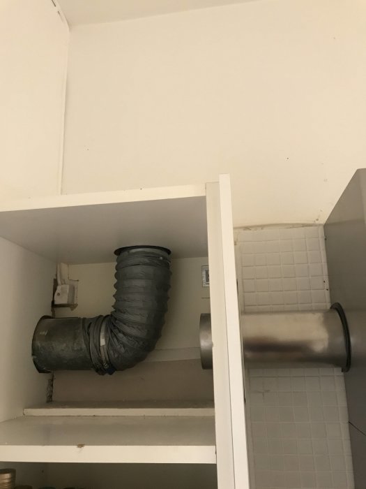 Flexibel ventilationskanal installerad ovanför köksskåp som leder bort från vägguttag.