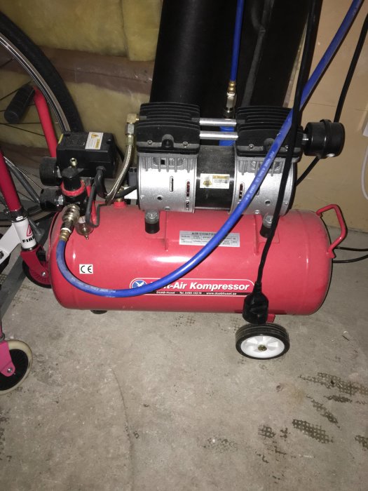 Röd portabel luftkompressor med kopplade slangar i ett garage.