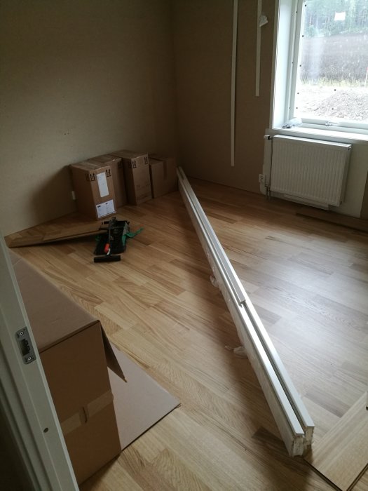 Nyinstallerat golv och omonterat trappstaket i ett rum under renovering med kartonger och verktyg.