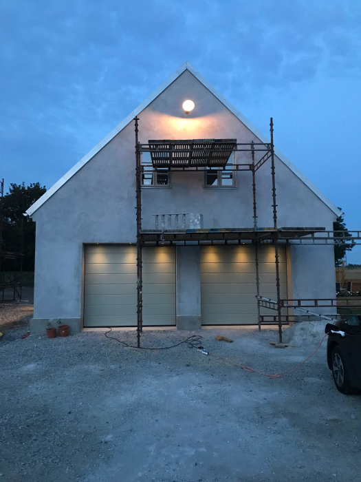 Hus under renovering med ställningar, oavslutad fasad och balkong, i skymning med månen ovanför.