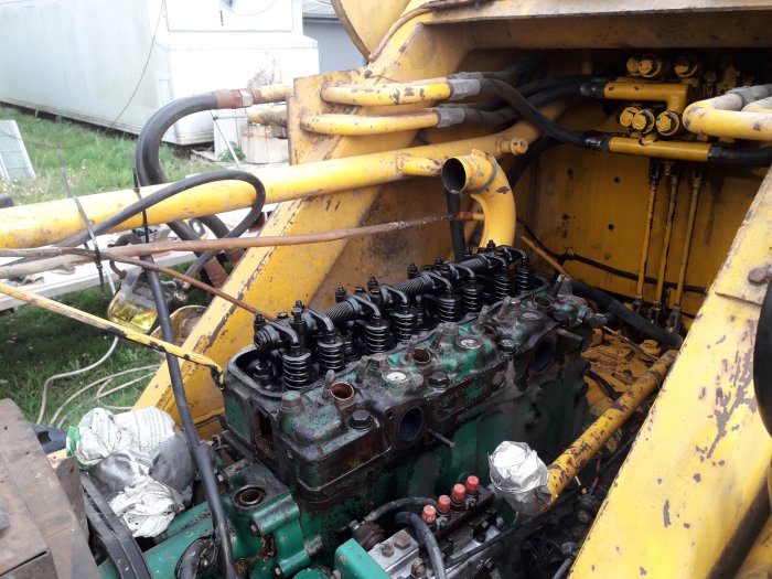 En öppnad motor på en gul baklastare, topplocket borttaget, visar ventilfjädrar och insprutningsrör.