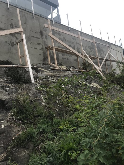 Utomhuspoolens gjutna betongmur med isolering av frigolit och fuktfläckar. Stödställningar syns framför.