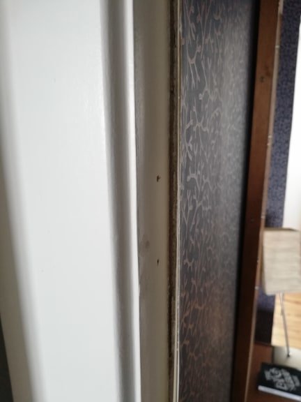 Glipa mellan en vit dörrkarm och mönstrad tapet där flera lager tapet skapar ojämn yta.