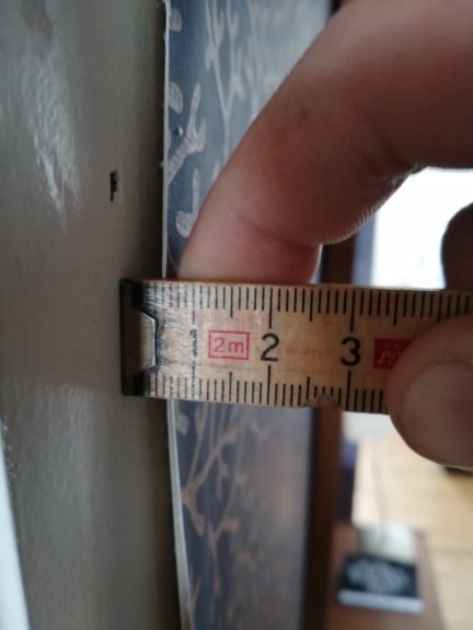 Finger som håller ett måttband mot en vägg för att mäta gapet mellan tapeten och dörrkarmen.