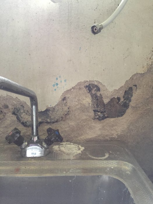 En källartvättstuga med putsade väggar där putsen börjat släppa, över en rostig diskbänk.