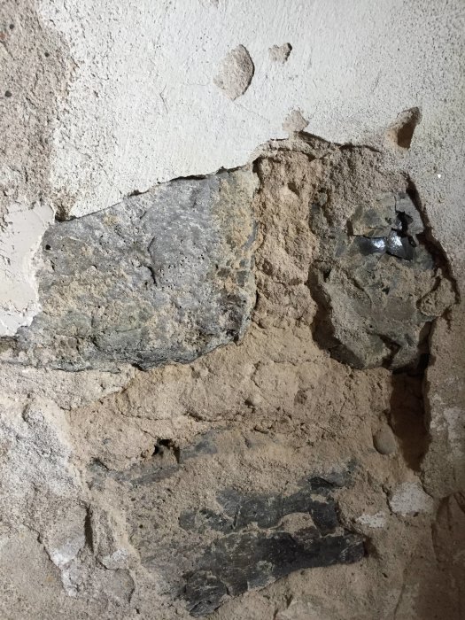 Putsad källarvägg där putsen delvis har släppt och avslöjat underliggande slaggsten.