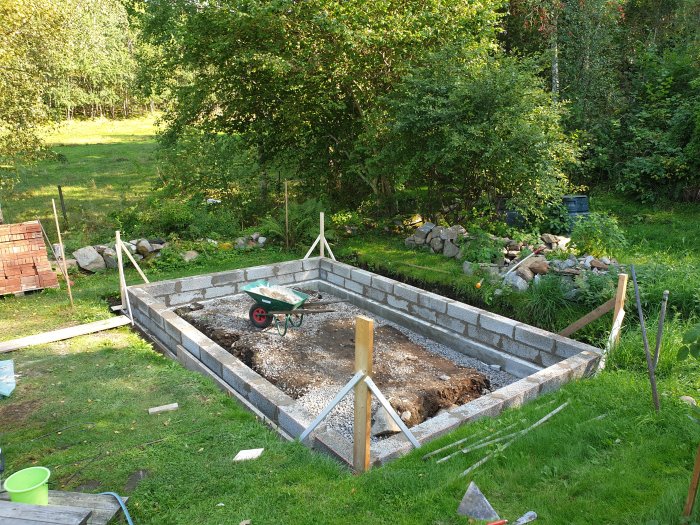 Grund av lecablockar för växthus under konstruktion med makadam och verktyg i en trädgård.