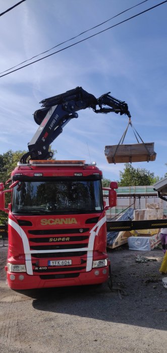 En kranbil av märket Scania lyfter takstolar för byggprojekt mot en klarblå himmel.