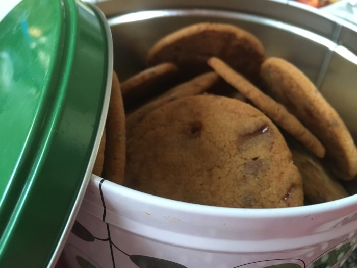 Hembakade tunna småkakor med chokladbitar i en kakburk.