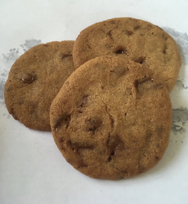 Tre hemgjorda sega småkakor med chokladbitar på pergamentpapper.