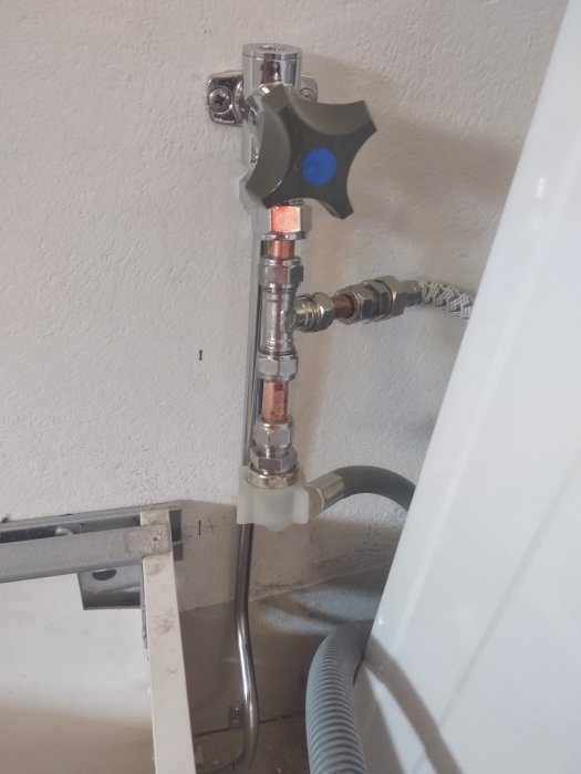 Installerad vattenanslutning med mässingskopplingar och avstängningsventil mot vit vägg.