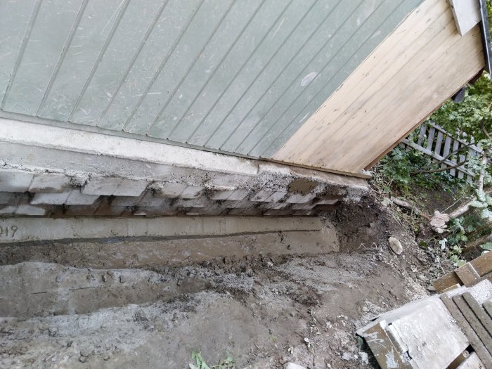 En avkapad betongklack vid en husvägg med synliga block och grus, redo för dränering och återfyllning.