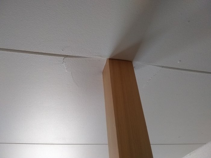 Spricka i innertaket vid en trästolpe, tecken på strukturell sviktning i byggnaden.