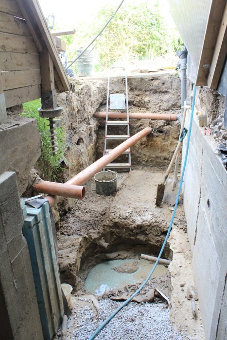 Grävplatsen vid husrenovering med synlig inspektionsbrunn, rörledningar och delvis gjuten bottenplatta.