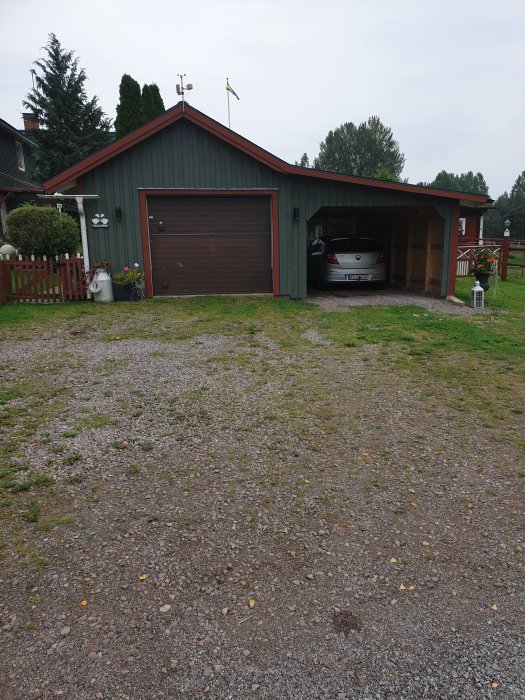 Ett grönt garage med en nyare mörkbrun garageport, bil parkerad inuti, framför grusuppfart.