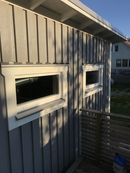 Exteriör av ett nyligen byggt hus med vertikal grå panel och vita fönsterkarmar i solnedgången.