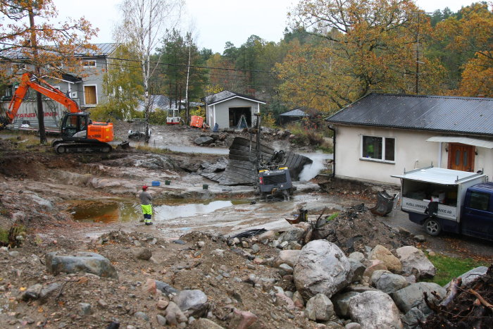 Byggplats med grävmaskiner och arbetare som förbereder sprängning intill hus.